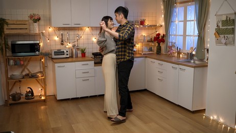 full length of happy asian couple hugging and dancing together while celebrating valentine’s day on romantic night date at a decorated home interior