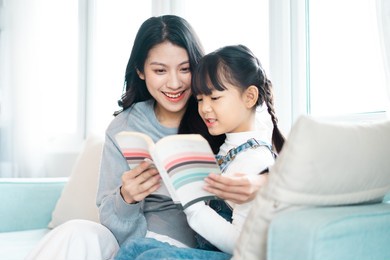image of mother and daughter sitting on the sofa reading a book