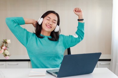 young asian happy woman with headphones relaxing stretching taking a break form online study on laptop, video call conference, education, internet and technology concept.