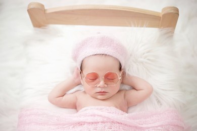 fashion baby girl with pink beret hat wearing fashion glass sleeping on bed with white fur.