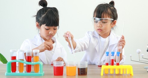 little girl asian cute little student child learning research and doing a chemical experiment while making analyzing and mixing liquid in test tube at home on the table.
