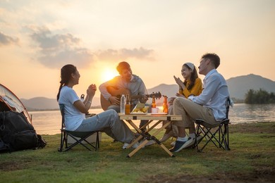 happy group of asian friends play guitar and sing enjoying camping and drinking beer