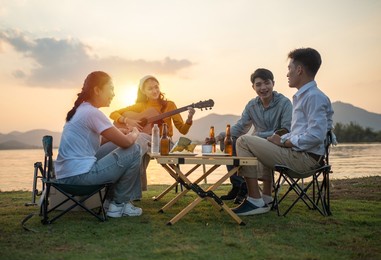 happy group of asian friends play guitar and sing enjoying camping and drinking beer