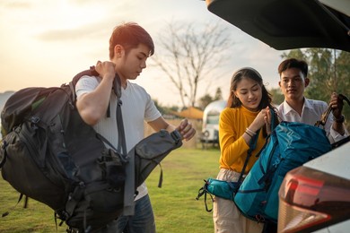 young man and woman helped to lift bag from the car to go to picnic in the summer holidays.they are happy and have fun on holidays.
