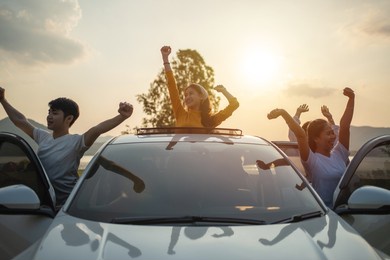 asian friends group in car travel and raise your hand cheerful excitement on sun roof with holiday destination. car travel