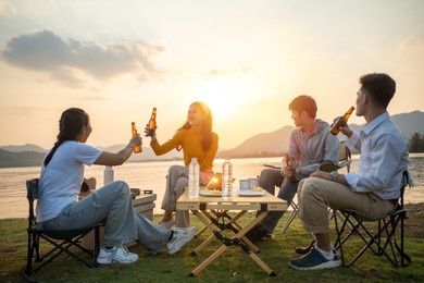 happy group of asian friends play guitar and sing enjoying camping and drinking beer
