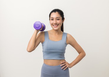 sporty asian woman exercises with dumbbells on isolated white background. good shape and health fitness woman weight training standing pose smile to camera.