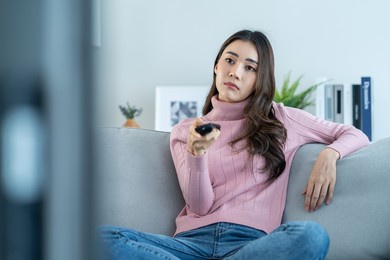asian unhappy young beautiful woman watch movie on television at home. attractive girl feel upset, sit on sofa in living room watch video on tv with boring face in house. activity lifestyles concept.