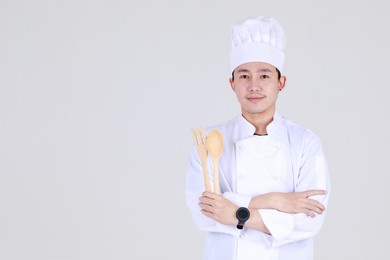 experienced and smart chinese chef on elegant cooking uniform smile and standing confidently at kitchen with arm crossed and spoon as qualified expert of cuisine for luxurious dining at restaurant.
