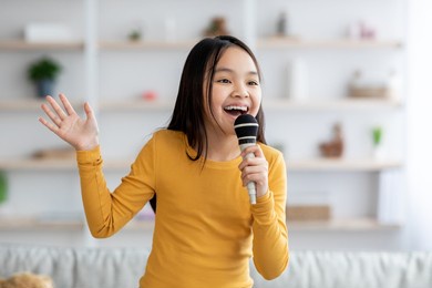 portrait of cute pretty long-haired korean girl teenager singing at home, using microphone and gesturing, looking at copy space. child singing karaoke, domestic entertainment for kids concept
