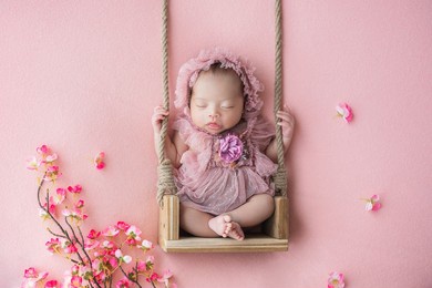 sleeping cute and adorable asian newborn baby sitting on swing with pink flower in background