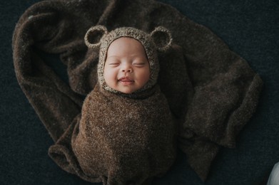 happy newborn baby wrapped in cocoon sleeping with cute knit bear hat