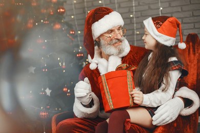 santa claus hugging children and giving them gifts and sitting near the christmas tree