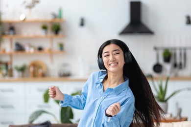 happy carefree asian young woman in headphones joyfully dancing alone having fun at home
