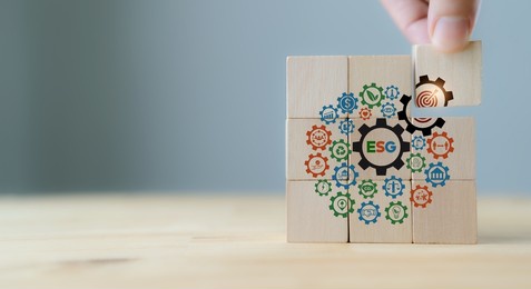esg concept of environmental, social and governance. sustainable corporation development. hand holds wooden cubes with esg target icon  standing with other esg icons on grey background. copy space.