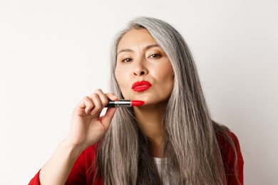 beauty and makeup concept. beautiful asian elderly woman pucker lips, showing red lipstick and looking sassy at camera, white background