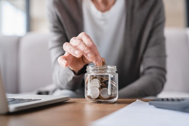 cropped focused shot. savings concept. nest egg of old elderly senior woman grandmother saving money, economizing pension, mortgage loan at home using laptop and putting coin into moneybox