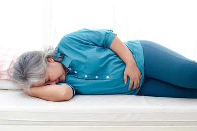 asian elderly woman has a stomachache. she lay on the white bed. elderly health concept. health insurance and elderly care