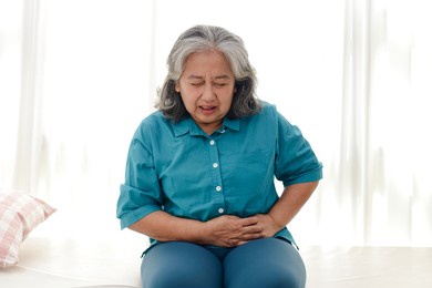asian elderly woman has a stomachache. she sat on the white bed. the concept of health care for the elderly. illness. health insurance.