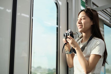 a beautiful asian female tourist with camera in the passenger cabin, traveling by sky train, taking snapshot photos when transporting in urban view, city lifestyle by railway, happy journey vacation.