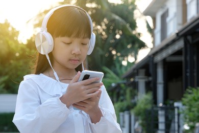 asian child girl uses headphones to listen to music on her smartphone in a good mood.