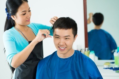 female hairdresser cutting hair of smiling male client at beauty salon