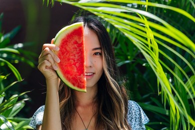 a portrait of a young adult east asian woman holding a slice of watermelon in a garden in bali, indonesia