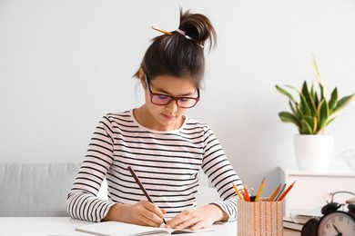 little asian girl writing in copybook while studying with online tutor at home