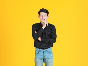 portrait studio shot of asian young man professional successful male businessman in casual black shirt standing smiling look at camera on yellow background