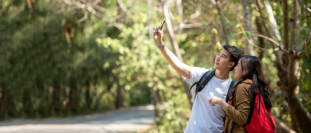 tourist and traveler asian couple backpack enjoy happy take a photo selfie in the jungle forest nature park . traveler going camping and explore outdoors destination leisure, copy space for banner