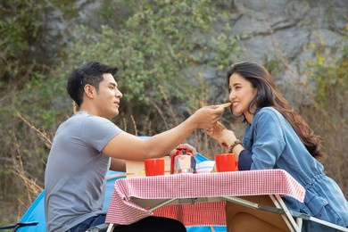 young asian couple having breakfast together in front of tent while camping in park
