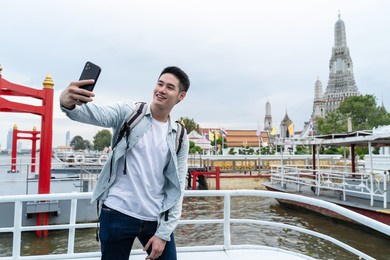asian young male backpacker use smartphone selfie take picture in city. handsome man tourist traveler wear mask travel alone on street, use smartphone record vlog on holiday vacation trip in thailand