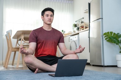 asian handsome active young man doing exercise on floor in living room. attractive male in sportswear spend leisure activity time to workout for health by follow online instruction on laptop at home.
