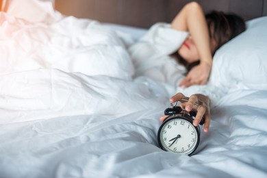 asian woman lying in bed at morning with retro alarm clock, young female sleep in bedroom at home. restless, insomnia sleeping, worried and stressed concepts