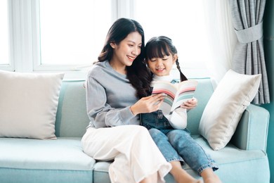 image of mother and daughter sitting on the sofa reading a book
