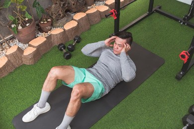 a fit asian man does abdominal crunches while lying on a black mat. working out his core at his home gym.