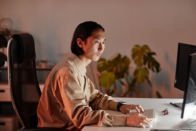 contemporary young asian businessman sitting in front of computer monitors while working late in openspace office