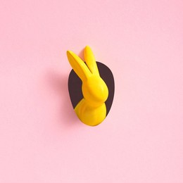 yellow easter bunny looks out of an egg-shaped hole in the pink background wall. abstract concept. square with copy space.