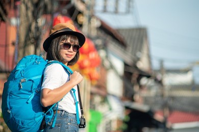asian woman walking travel backpack in city. digital tourism concept. woman traveling with backpack and straw hat use smartphone to take pictures.