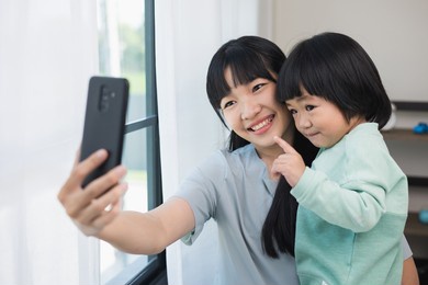 mom carry son using smartphone video call to say hi with family stay at home. mother holding little boy hugging shared happy moment on social media walking in living room.