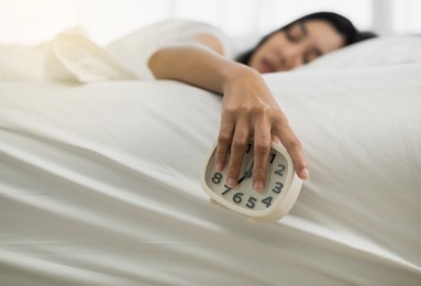 beautiful woman is awakened by an alarm clock in bed in the morning. young asian woman doesn't want to wake up and doesn't like the sound of an alarm clock.