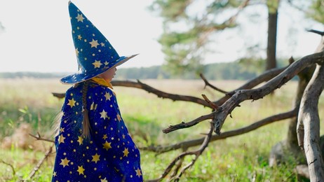 fantasy child in wizards robe in forest. kid play magician outdoors. girl, kid, plays in wizard costume in spring in forest, studies dry tree. halloween. happy childhood, family. child playing in park