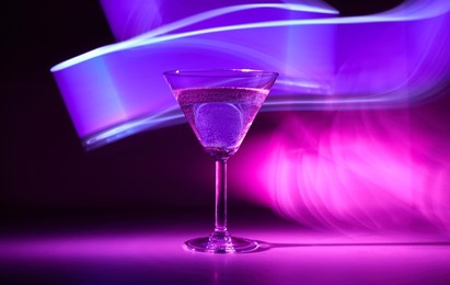 martini cocktail drink with ice cubes in neon iridescent pink and blue colors. minimal night party life and juzz concept. background painted with light