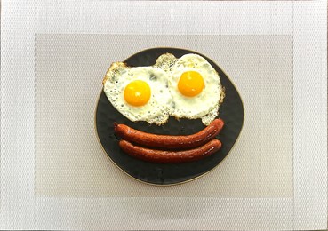 top view of fried egg and sausage smile face on black plate in white table, breakfast serve for kid, funny breakfast. high quality photo