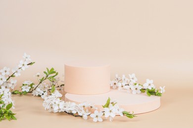geometric podium platform stand for product presentation and spring flowering tree branch with white flowers on pastel beige background. front view