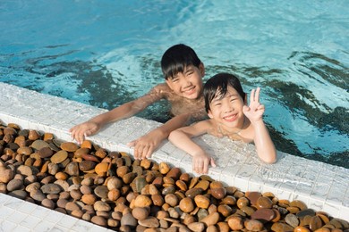 asian young boy brother having a good time playing and enjoying in swimming pool together in summer