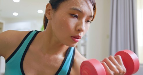 beautiful athletic asian woman is sweating while training with dumbbell at home