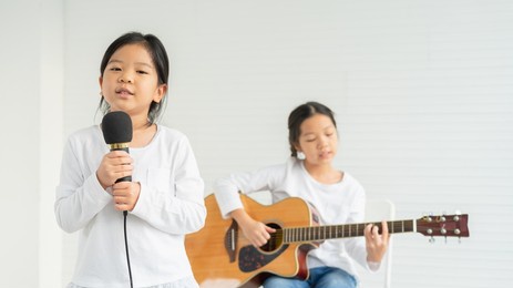 cute little children show singing look at camera with young child playing guitar at background. asian children study and learn musical and singing in education classroom at small school