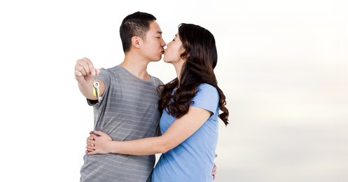 composite image of asian couple holding house keys kissing against white background. real estate concept