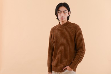 fashion model. young man with hairstyle in sweater posing in studio on brown background

